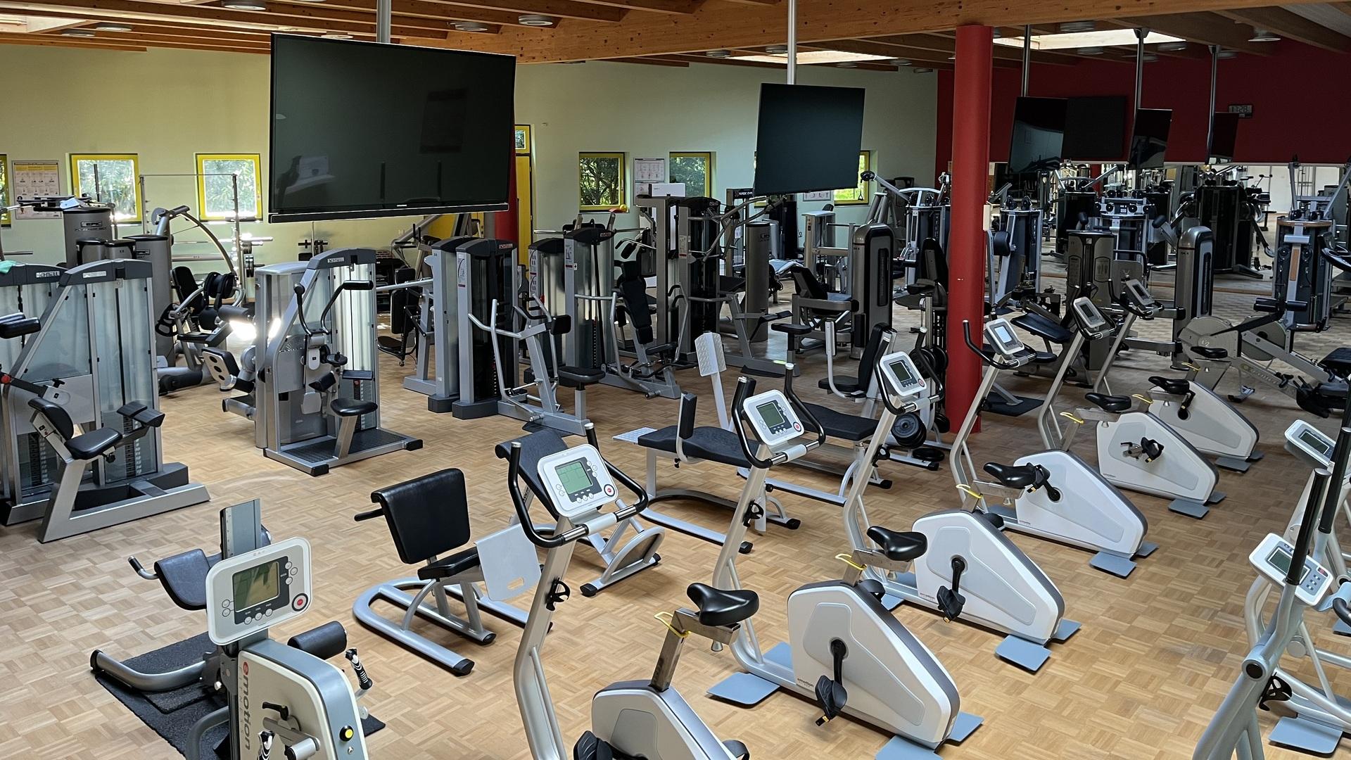 Fitnessstudio mit verschiedenen Trainingsgeräten, darunter Laufbänder und Krafttrainingsmaschinen, in einem hellen Raum.