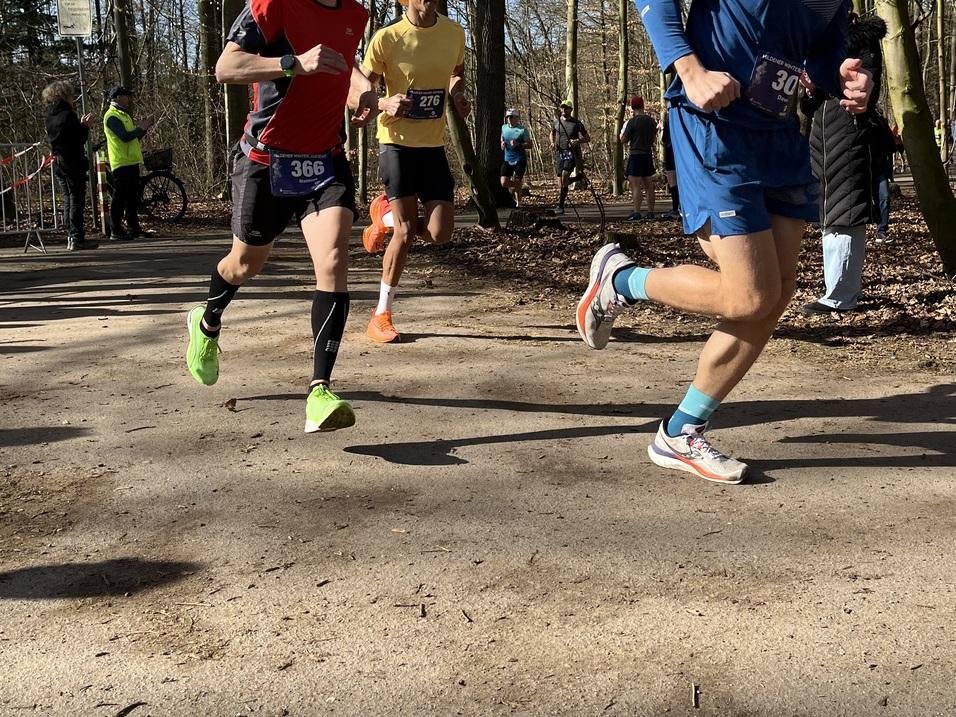 Zwei Läufer in Sportkleidung beim Wettlauf auf einem Waldweg, umgeben von Zuschauern und weiteren Teilnehmern.